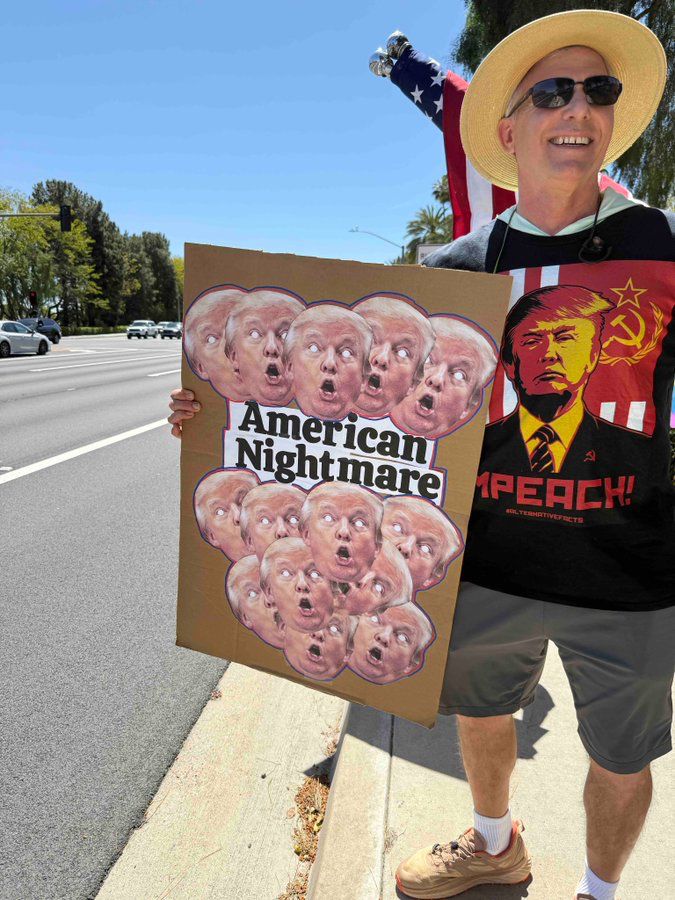 Smiling middle-aged man in shorts, athletic shoes, sun hat, and an Impeach Trump t-shirt, carried homemade sign along busy road. The sign has 14 identical photos of Trumps head with his mouth open, and his eyes completely white, and the words "American Nightmare."