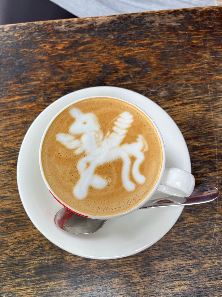 A porcelain cup containing a flat white topped with steamed milk in the shape of a winged unicorn. 