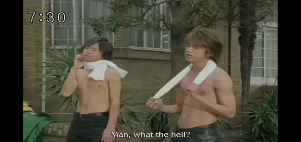 Screenshot from Stage 10 of Mahou Sentai Magiranger: Brothers Kai and Tsubasa Ozu are shirtless with white towels around their necks, standing in the courtyard of their family home, annoyed at their brother Makito offscreen.
Tsubasa has a lean, muscular build.