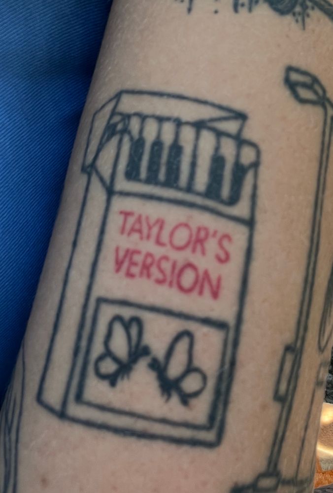 Tattoo of a cigarette box with piano keys instead of cigarettes. On the outside of the box there’s is “Taylor’s Version” in red ink and two butterflies 