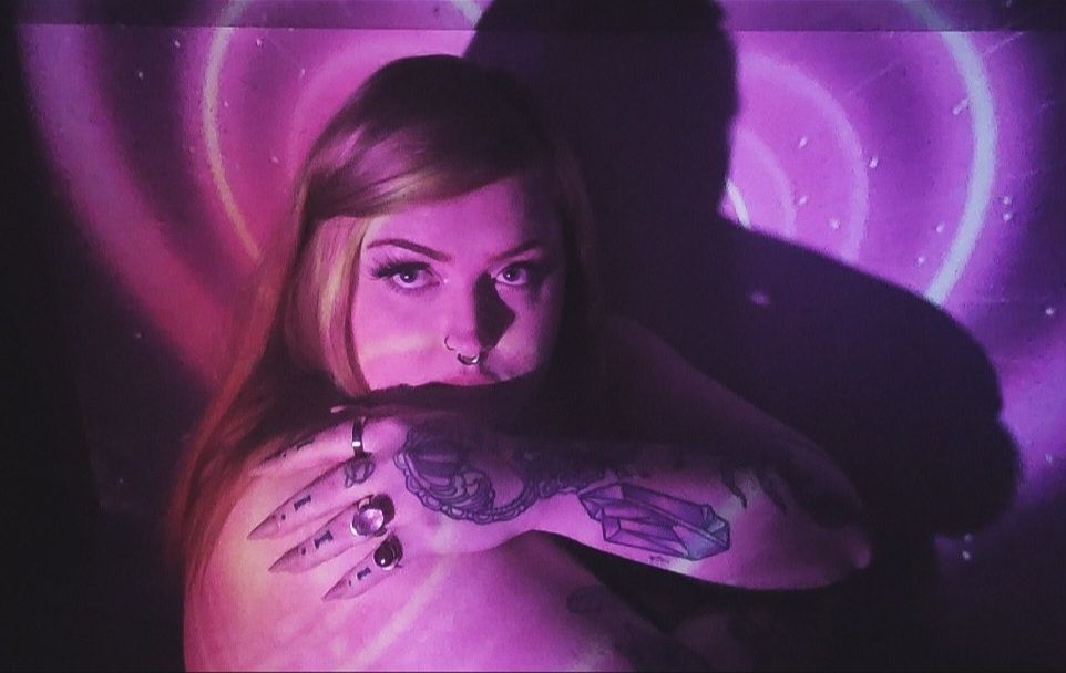 portrait of a red haired girl with tattoos sitting infront of a projector showing a heart tunnel