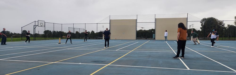 A pickup game of cricket being played on a netball court