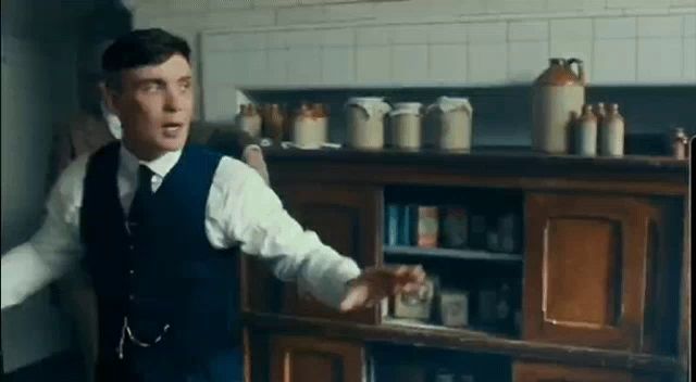 a man in a suit and tie is standing in front of a wooden cabinet in a kitchen .