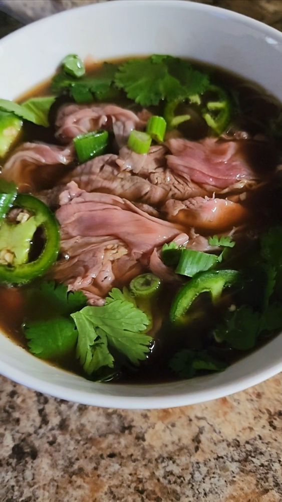 A bowl of pho bo, a Vietnamese noodle soup with rice noodles, thinly sliced steak, and a rich beef broth, garnished with scallion, cilantro, and jalapeno.
