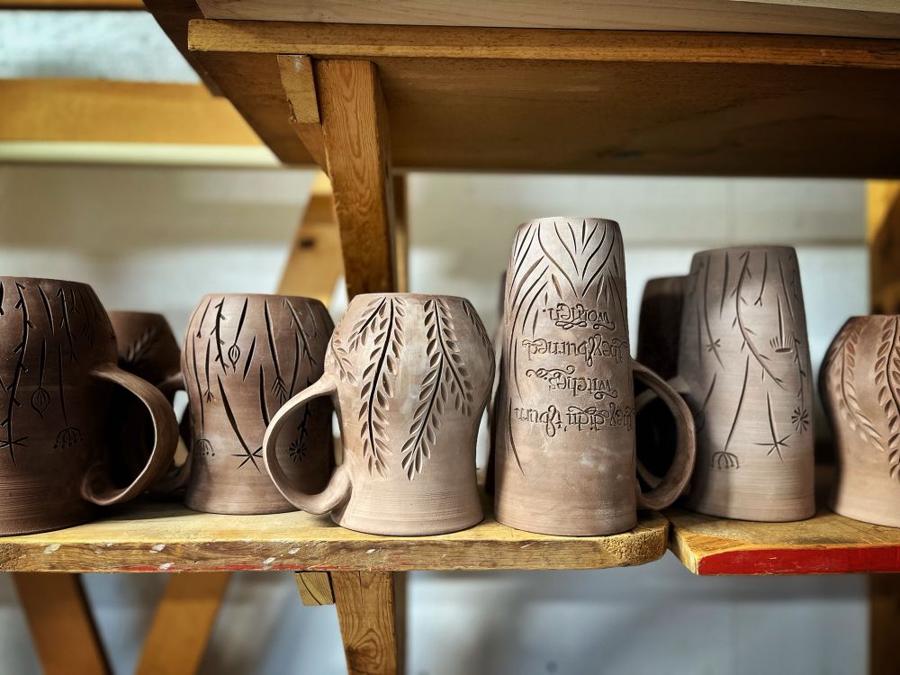 A variety of hand-carved greenware mugs drying on a shelf. 