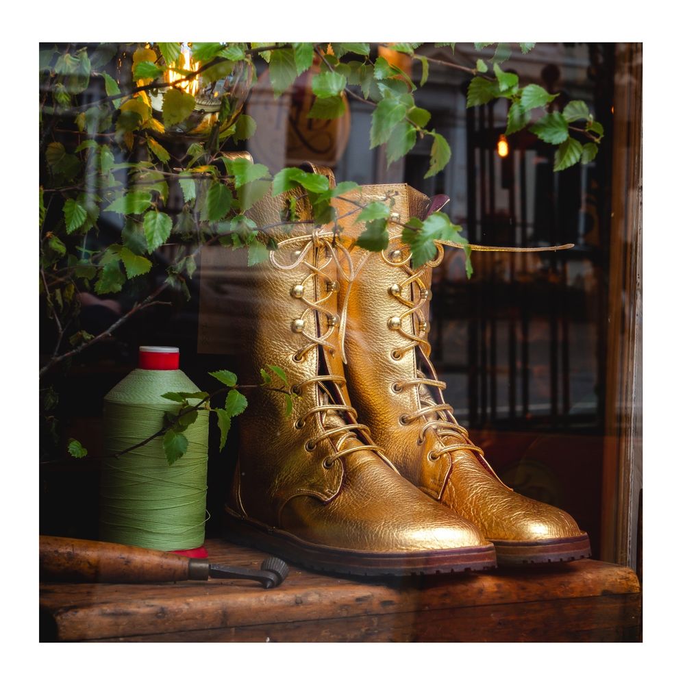 A pair of gold Dr Martin stye boots in a shop window next to a spool of green yarn and adorned with Holly leaves