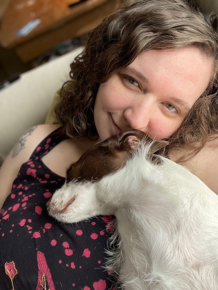 Selfie of woman with brown curly hair, and a brown and white jack Russell-mix dog asleep on her chest 