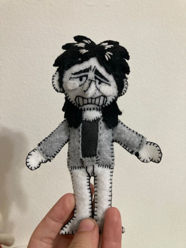 A Kaiji Itou made out of grey, white, and black felt. He is crying. He design is like paper Mario, and he is outlined in a blanket stitch 