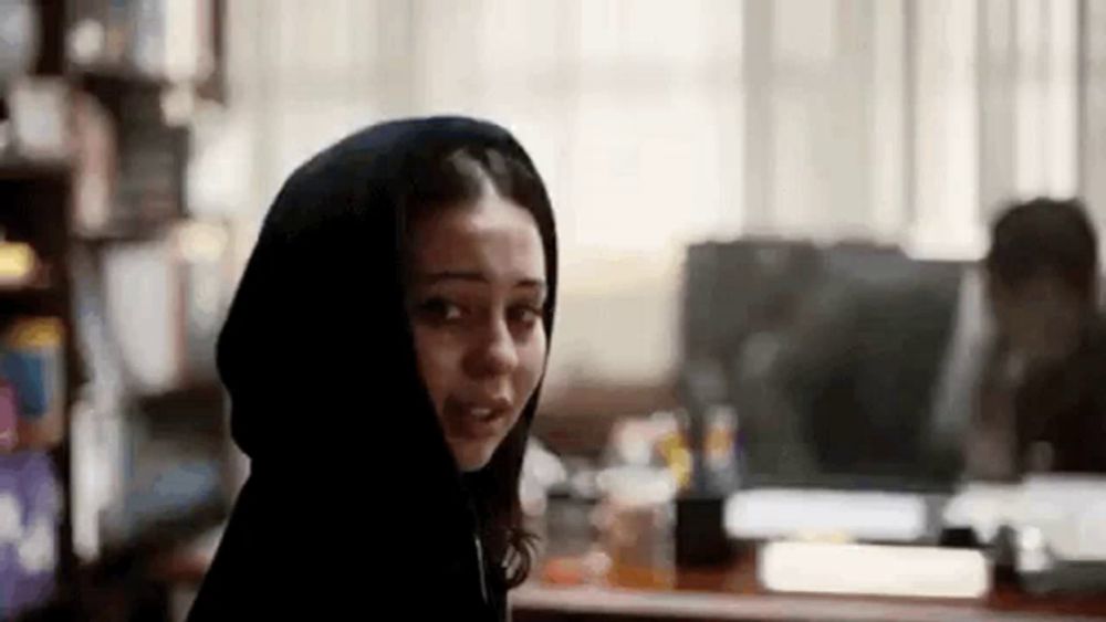 a woman in a hooded jacket is looking at the camera in a library .