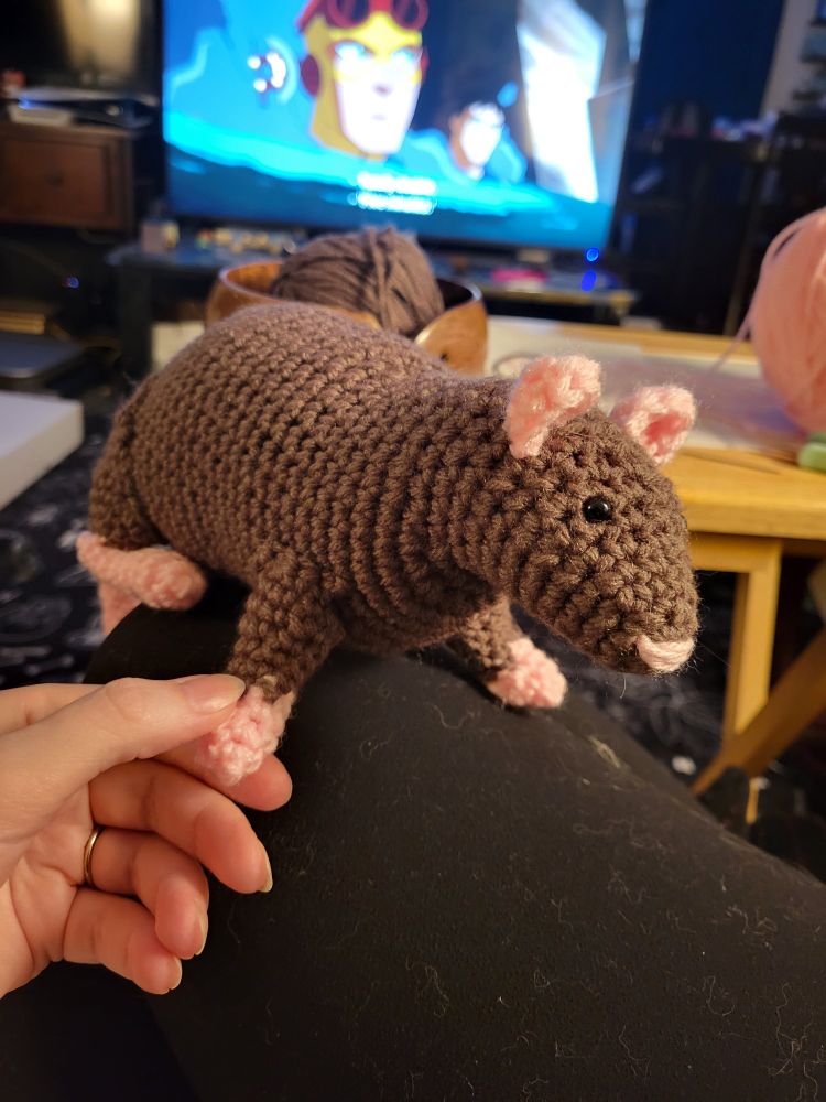 A brown crocheted rat with cite pink feet