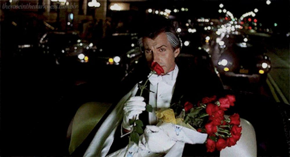 a man in a tuxedo and white gloves is holding a rose