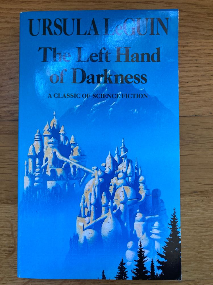 Picture of the front cover of LeGuin's The Left Hand of Darkness showing two domed & spired cities atop forested peaks with a mountain in the background.  