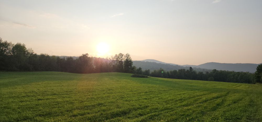 Still a lot of smoke in the air between us and the not too far away ridgelines. Orange sunset over a field.
