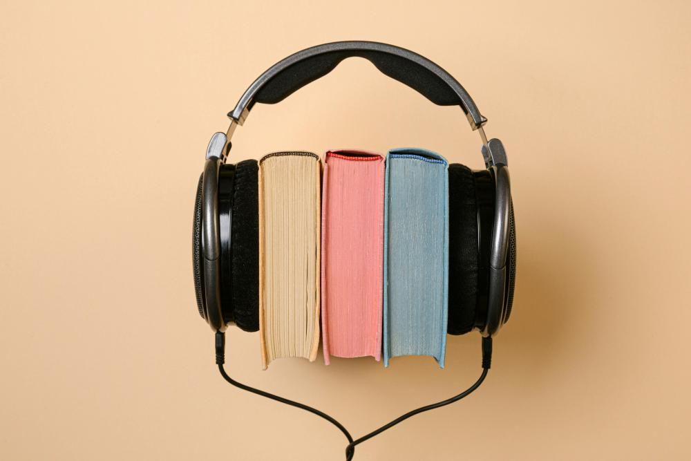 Three books, colored yellow, red, and blue, between a pair of over-the-ear headphones.
