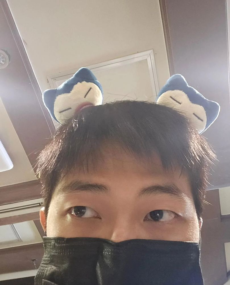 Namjoon (RM of BTS) taking a selca of himself wearing a Snorlax (Pokémon) headband. He's also wearing a black face mask