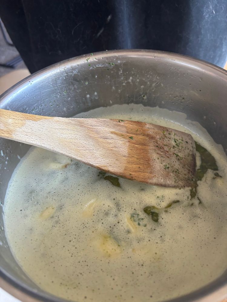 Knoblauch wird in Butter karamellisiert, man sieht einen Topf mit Holzkochlöffel und schäumende Butter in der Knoblauchzehen schwimmen
