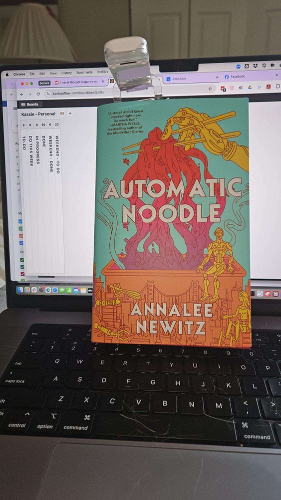 A copy of "Automatic Noodle" by Annalee Newitz propped up on a laptop keyboard with a to-do list showing on the screen behind it.