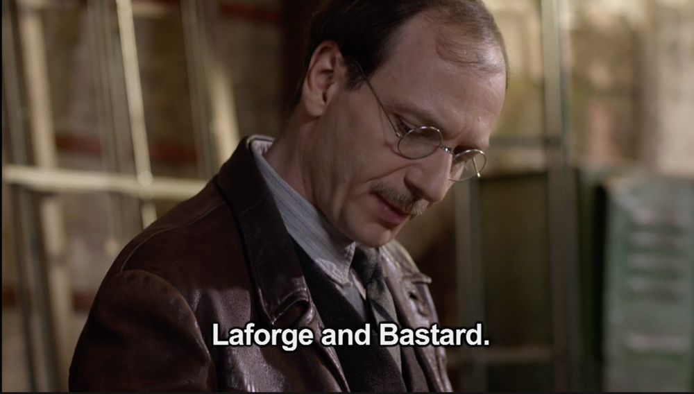 A scene from the French WWII drama "A French Village" showing a man with glasses reading from a list of people arrested by the Nazis.
