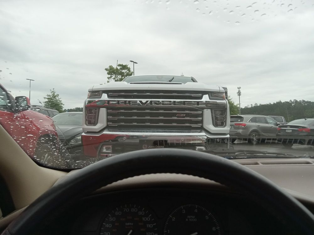 The front of a monstrous, production Chevy truck as seen from a normal car. The grille is so tall that the bottom 3/4 of the windshield is obstructed.