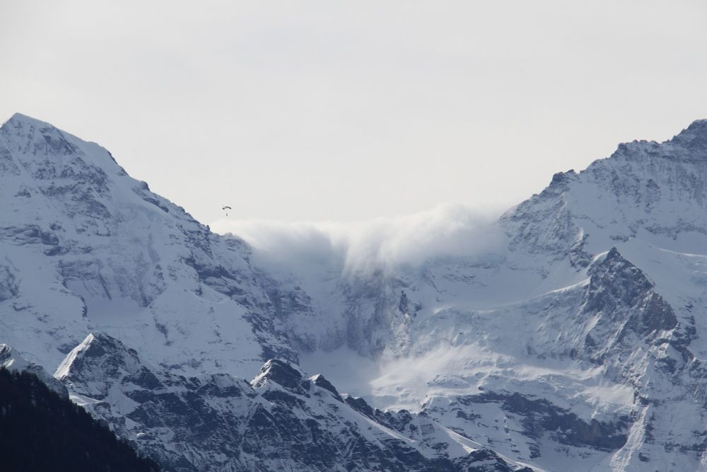 Un parapentiste vole au-dessus d'un massif montagneux enneigé, englouti par les nuages, dans la région d'Interlaken en Suisse.