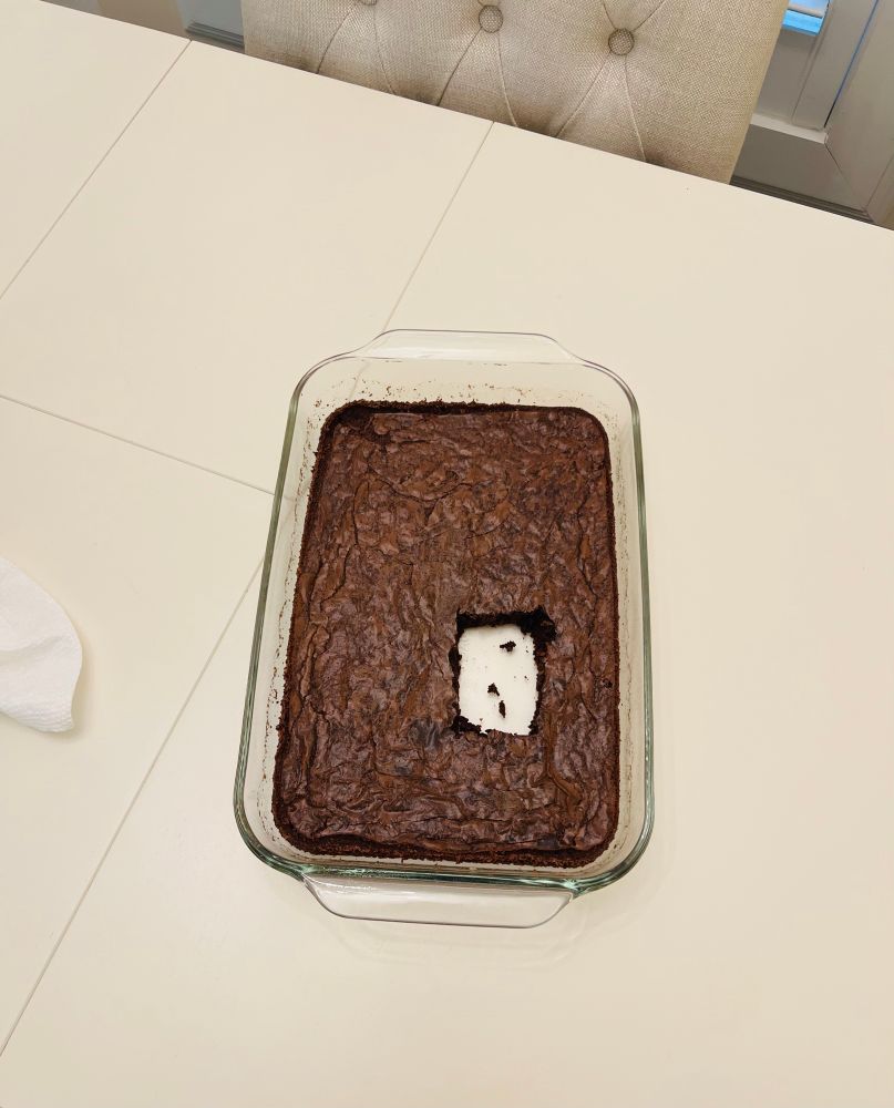 A pan of brownies with a piece cut out of the near middle. 