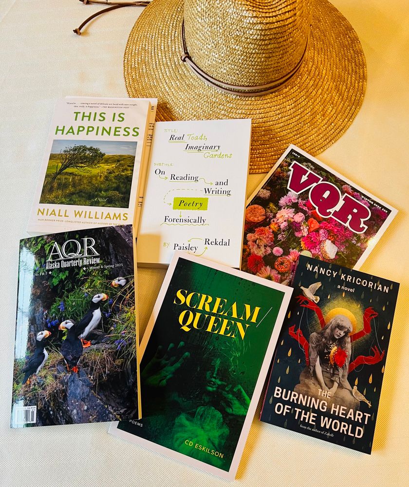 Collection of books spread out on a cream colored surface under my sun hat: THIS IS HAPPINESS, REAL TOADS IMAGINARY GARDENS, Latest issues of VQR and AQR, SCREAM QUEEN, THE BURNING HEART OF THE WORLD 