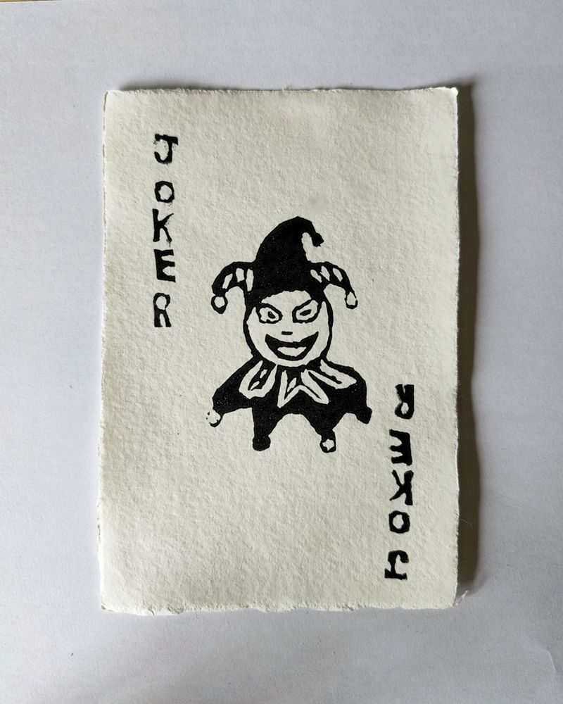 Linocut print of a Joker card, in the style of a Joker from the digital card game 'Balatro'. Printed on off-white, rough, textured paper.