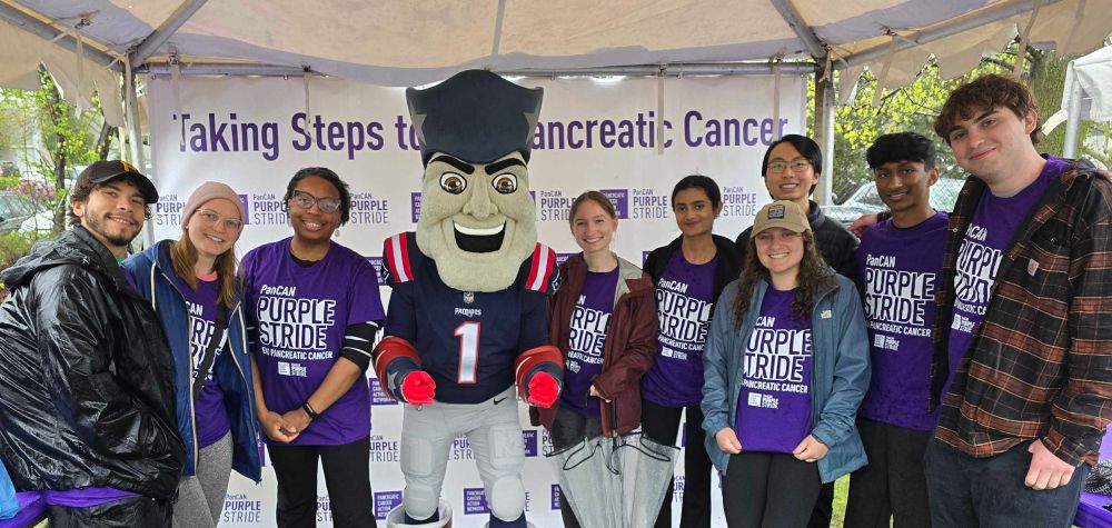 Pratt Lab members pose while wearing matching PurpleStride t-shirts. The backdrop overhead states "Taking Steps to End Pancreatic Cancer."