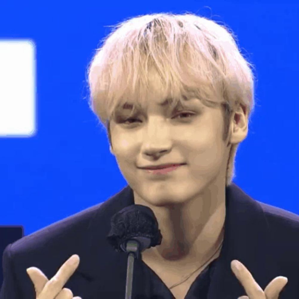 a young man with blonde hair is giving a peace sign while standing in front of a microphone