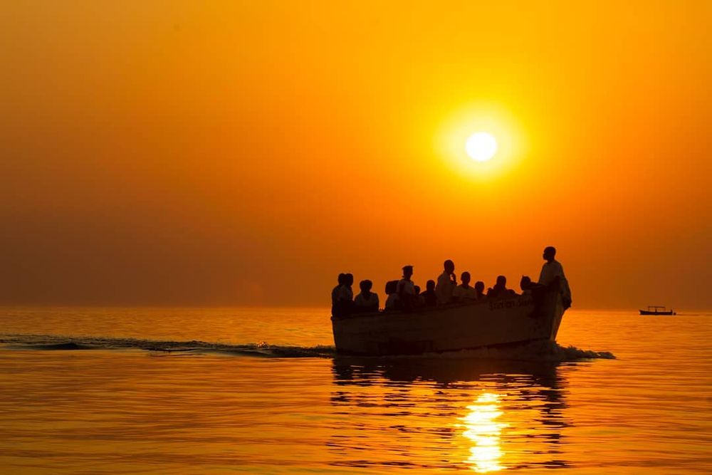Wooden boat full of people going across the water during sunset