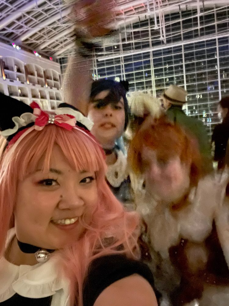 Hilda, Felix and sylvain cosplayers dressed as maids taking a selfie, only hilda is in focus and smiling. 