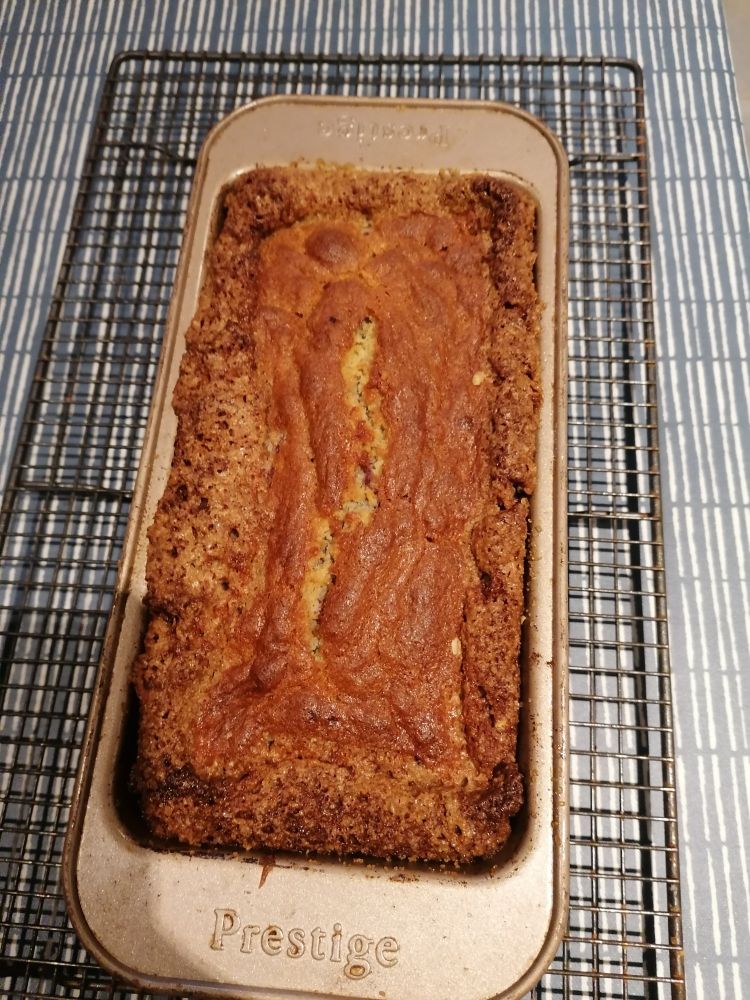 A loaf tin containing a very delicious looking banana bread. The edges are all crispy with caramelised sugar. 