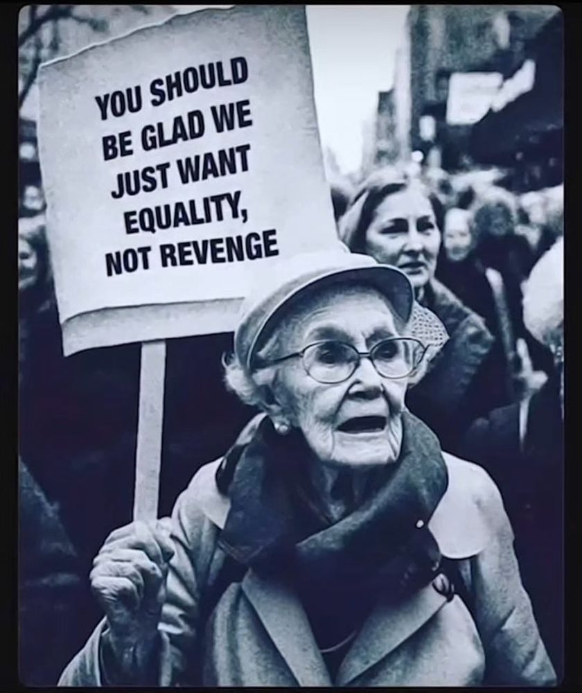 Elder woman in a demonstration carrying a placard saying ‘You should be glad we just want equality and not revenge.’
