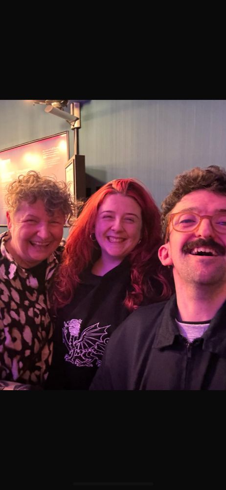 smiling joyful faces as friends O’Reilly, Poppy and Macsen meet unexpectedly in theatre bar
