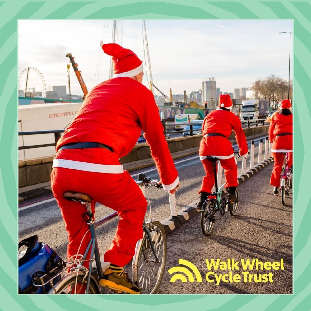 3 cyclists in Santa costumes cycling over a bridge in a city.