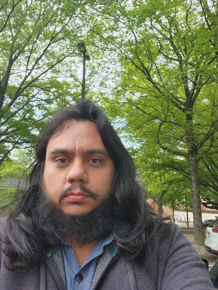 Selfie while wearing a hoodie with my beard and long hair on display. Attempting a smile