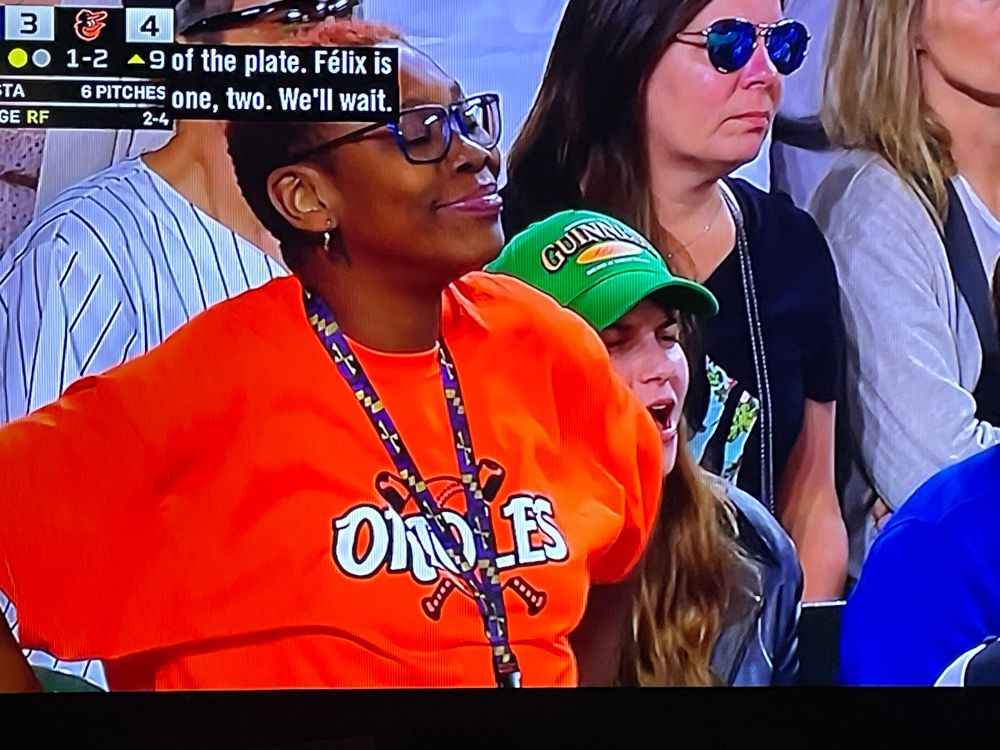 Black women fan wearing orange Orioles shirt making satisfied face at Bautista pitch