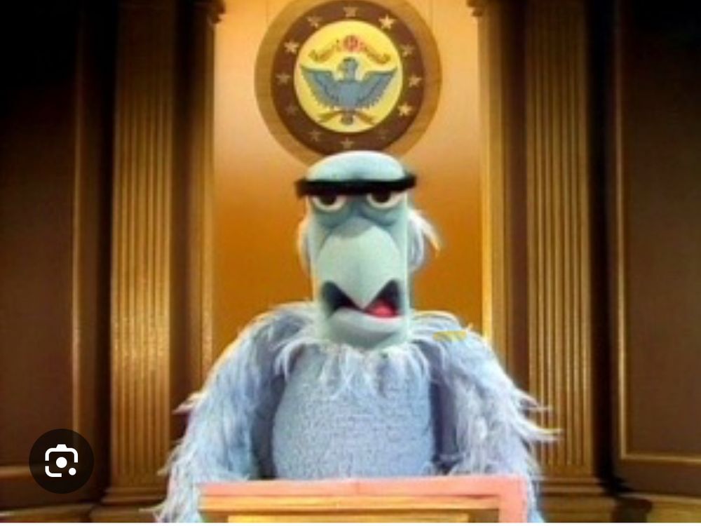 Sam the Eagle at a podium with an American Eagle seal on wall behind him