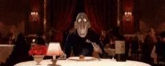 a cartoon character is sitting at a table with a fork in his mouth .