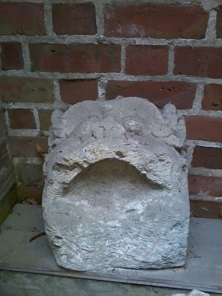 A limestone Mascaron of a beastly humanoid face, smiling with a huge open mouth.
