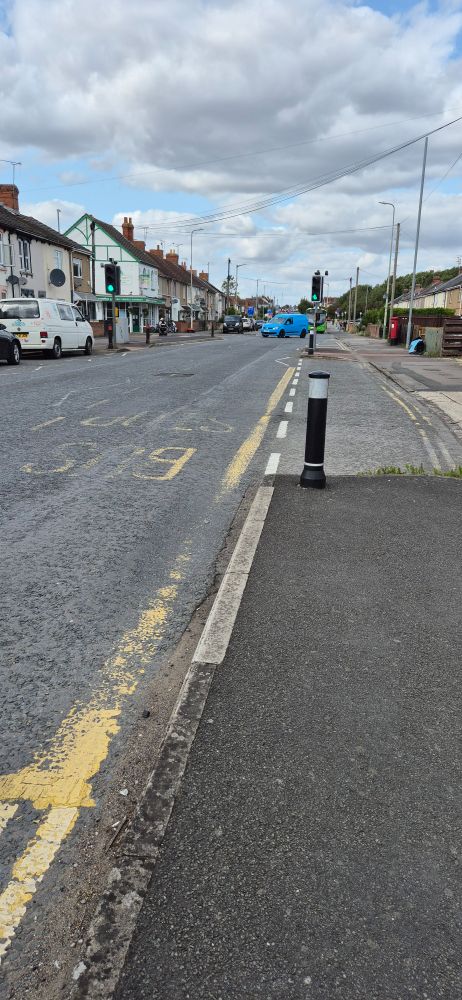 A photo of the area where I'm waiting for a bus. It's a run-down area of Swindon in the UK, and a blue car is visible turning into a side street. I'm surprised there isn't a smouldering car in view, for a change.