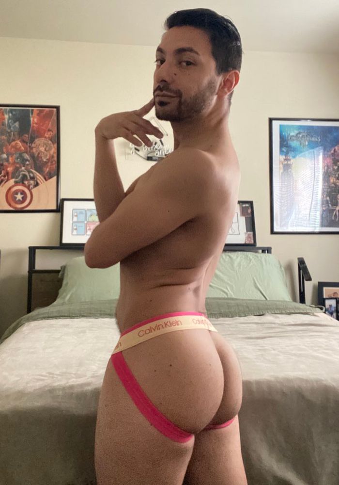 Selfie of me in my bedroom, wearing a pink and gold jockstrap, facing away from camera.