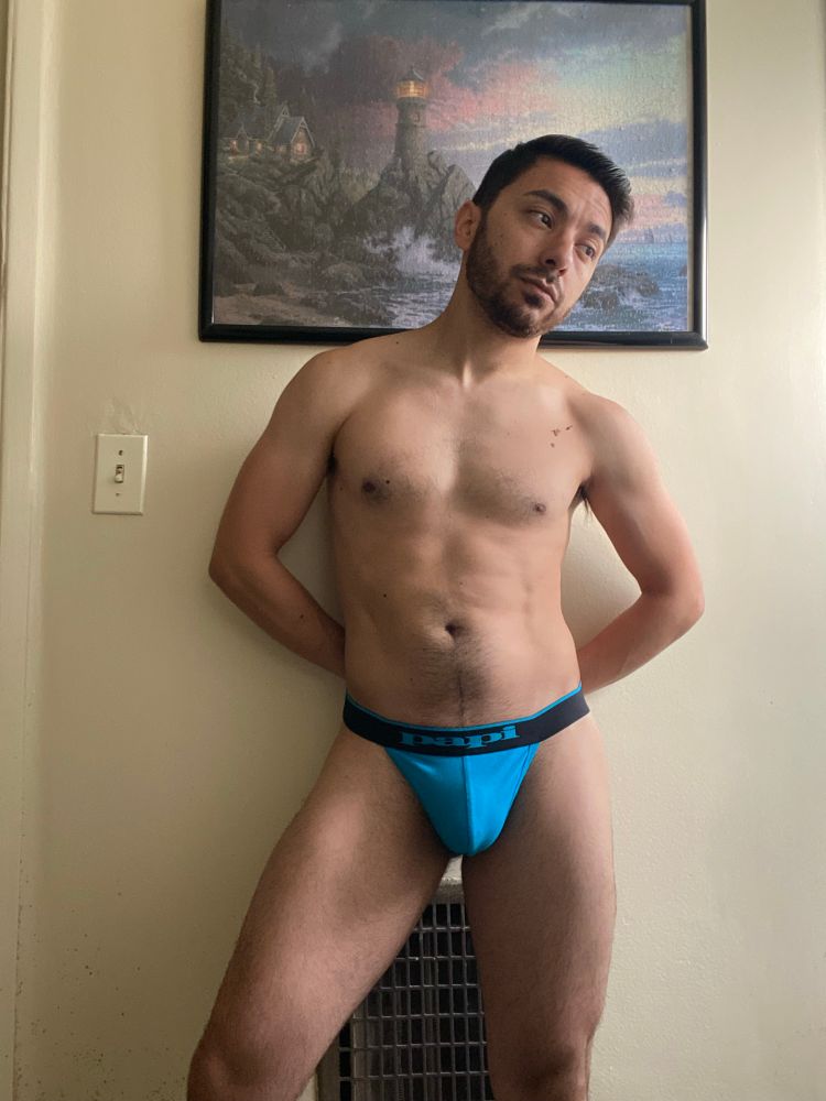 Selfie of me in bathroom, shirtless in a blue Papi thong, with my hands behind my back.