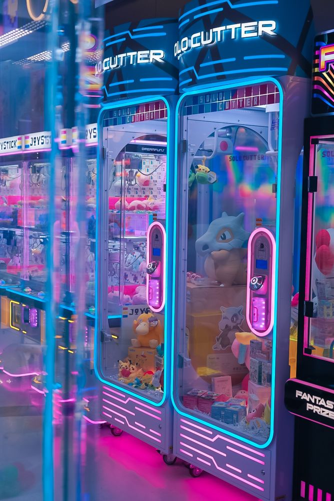 A photo of a brightly lit and coloured arcade machine. The lights are a mix of real and bright pink. There are Pokemon prizes in the machine.
