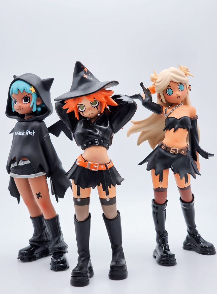 A trio of cute, punky femme figures. They're dressed in witchy black outfits with chunky boots and lots of cute accessories.