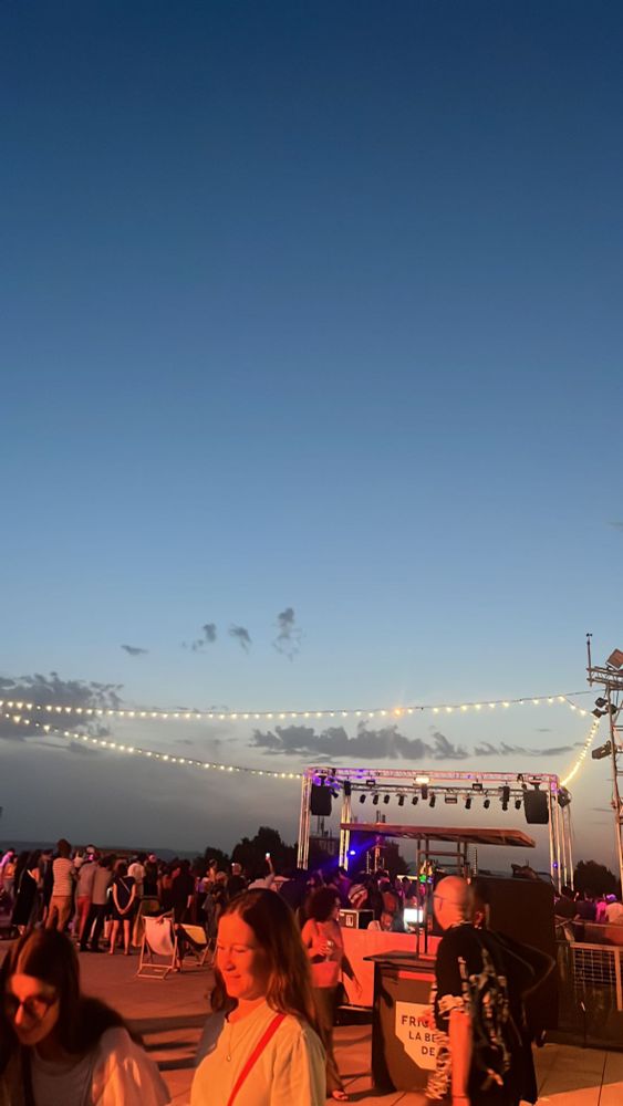 DJ set sur le toit de la Friche. Crépuscule, guirlande lumineuse, quelques spectateurices dans une lumière rouge.