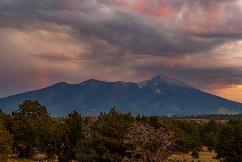 Dark grey and orange sunset clouds in fun shapes in the high desert with mountains in the middle distance