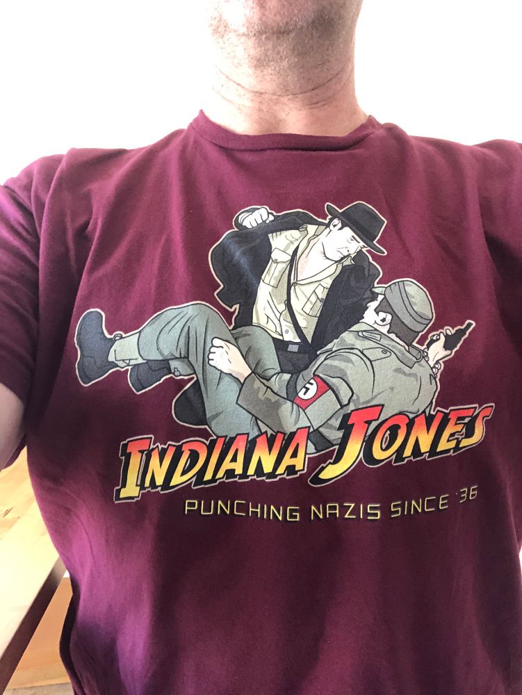Photo of a tshirt with a picture of Indiana Jones pinching a Nazi. Text on the shirt says: “Indiana Jones: Punching Nazis since ‘36”