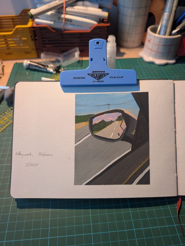 Photo d'une peinture à la gouache. Peinture d'une vue d'un rétroviseur latéral gauche de voiture pris depuis l'intérieur de la voiture. Dans le retro on voit le coucher de soleil avec un ciel rose et violet