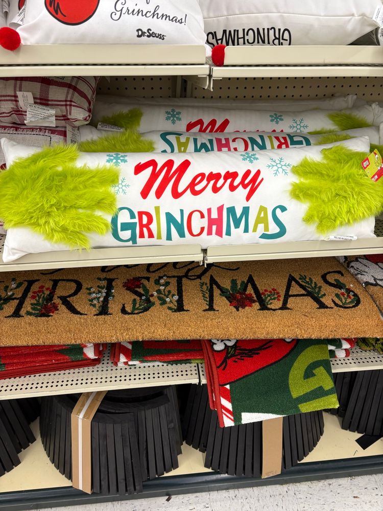 A pillow that says merry grinchmas with grinch hands holding it 